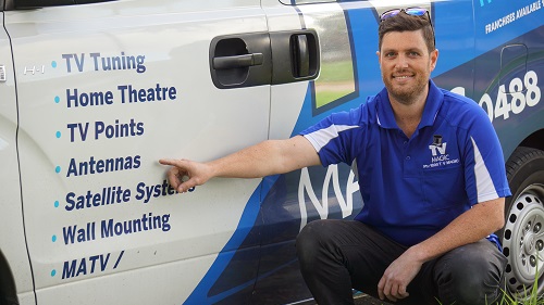 technician kneeling down next to his TV Magic van pointing to antennas service on the side of the vehicle