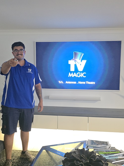 Technician with TV remote, in front of a TV he installed.