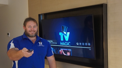 Technician with a TV remote in hand in front of a wall mounted TV