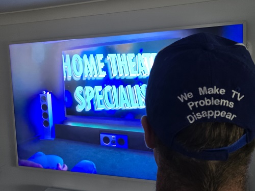 Back of technician's hat - in front of TV with "Home Theatre Specialists" caption