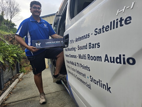 Technician holding a TV Magic wall bracket - standing next to his van.