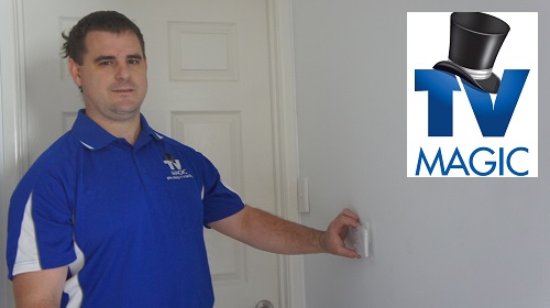 Technician holding up a TV point to a wall. TV Magic logo in top right corner