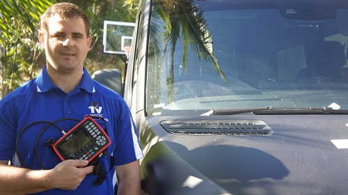 Technician holding a signal meter next to his TV Magic van