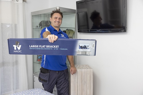 Technician holding up a custom TV Magic wall bracket, standing in front of a wall mounted TV.