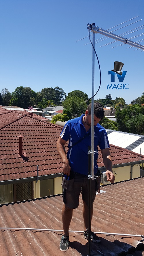 Technician installing an antenna on a tile roof. TV Magic logo in top right corner