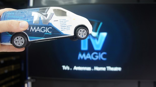 Close of of a TV with TV Magic logo on screen. Technician holding a mini TV Magic van in front of it.