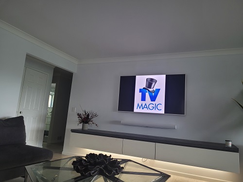 a wall mounted TV in a living room, with a TV Magic logo on the screen