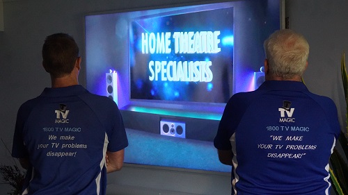 Two technicians with back facing out, in front of a screen that says "Home Theatre Specialists"
