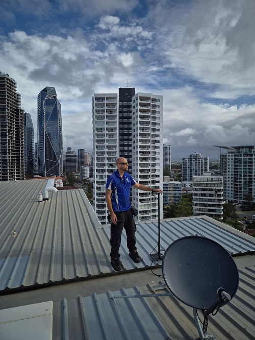 A technician on the roof of a building next to a satellite dish installation