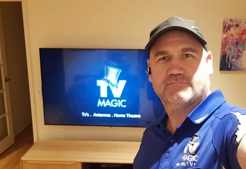 technician Doug in front of a wall mounted TV, with TV Magic image on screen of TV