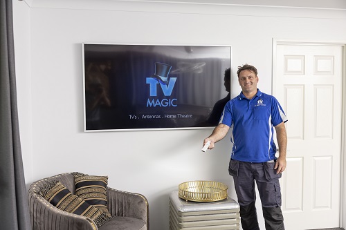 Technician standing holding TV remote in front of a TV he wall mounted