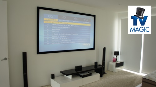a complete home cinema - projector screen, tower speakers, neat and tidy setup. TV Magic logo
