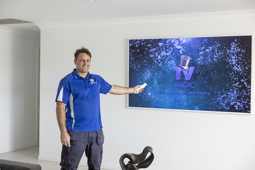 Technician pointing a remote at a TV he just installed. TV Magic logo on screen