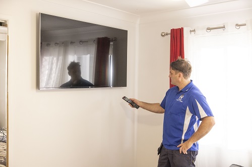 Technician with remote in front of wall mounted TV.