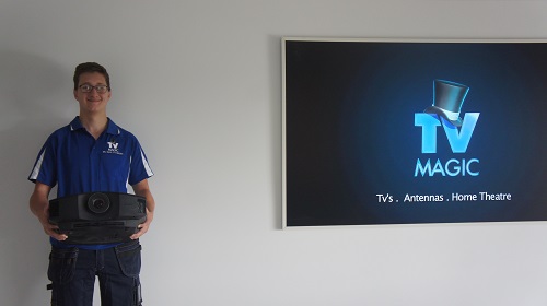 Technician holding a projector next to a large screen with TV Magic logo.