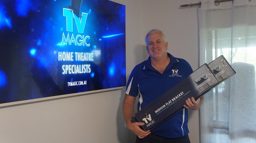 Technician - Steve, holding a wall bracket, next to a wall mounted TV
