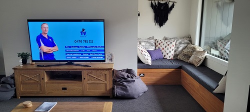 a TV on a display cabinet in a cosy living room. Technician displayed on the TV screen, with a list of his services