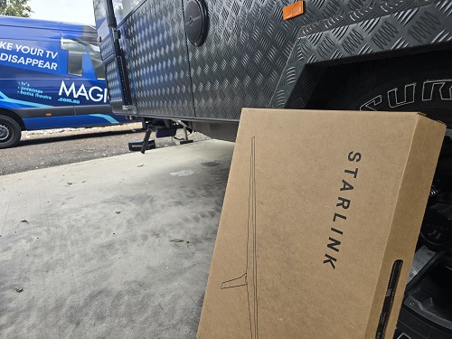 Starlink kit leaning on side of caravan. TV Magic van behind it.