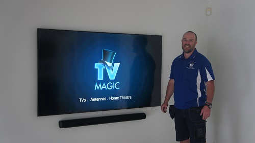TV Magic technician next to a wall mounted TV with floating sound bar