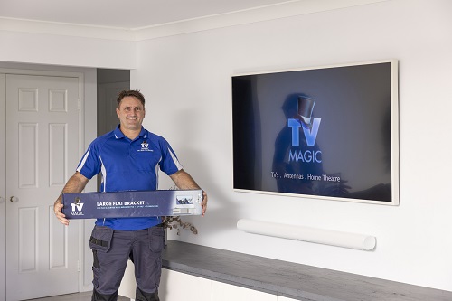 Technician holding a wall mounting bracket, in front of a large TV mounted on the wall