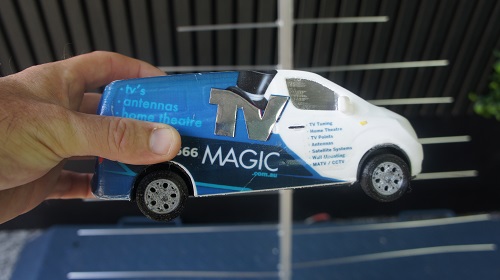 a Technician's hand holding a mini TV Magic van in front of an antenna