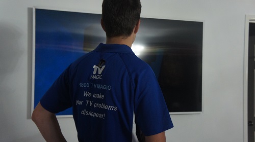 Technician in front of TV, with back of TV Magic shirt showing
